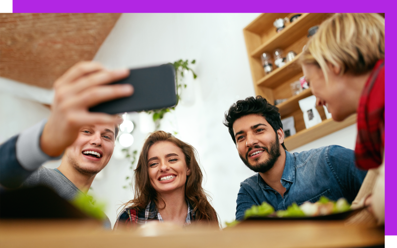 four employees taking a selfie with one smart phone and smiling in a workspace