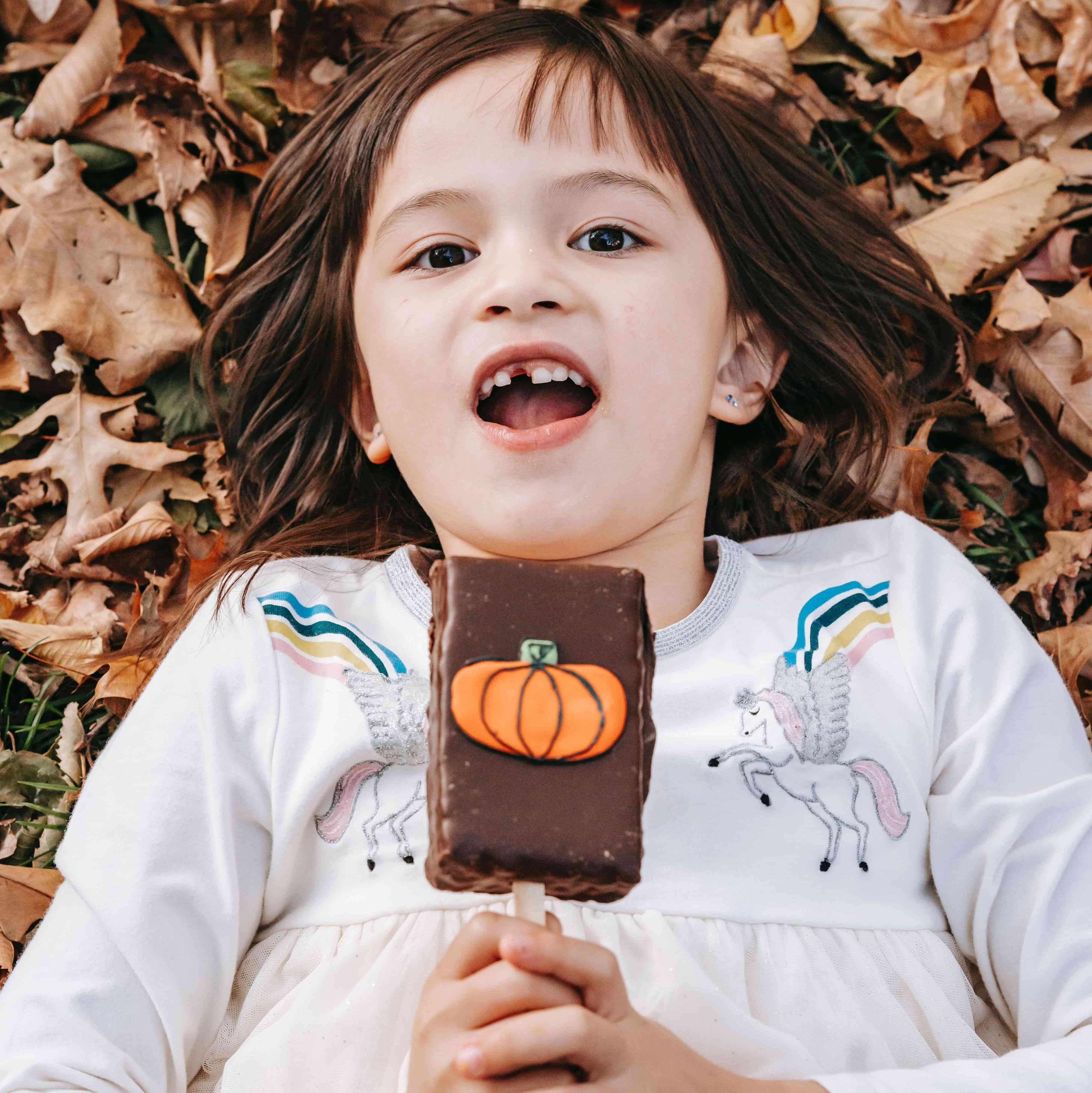 Child smiling and holding a chocolate with a pumpkin decoration