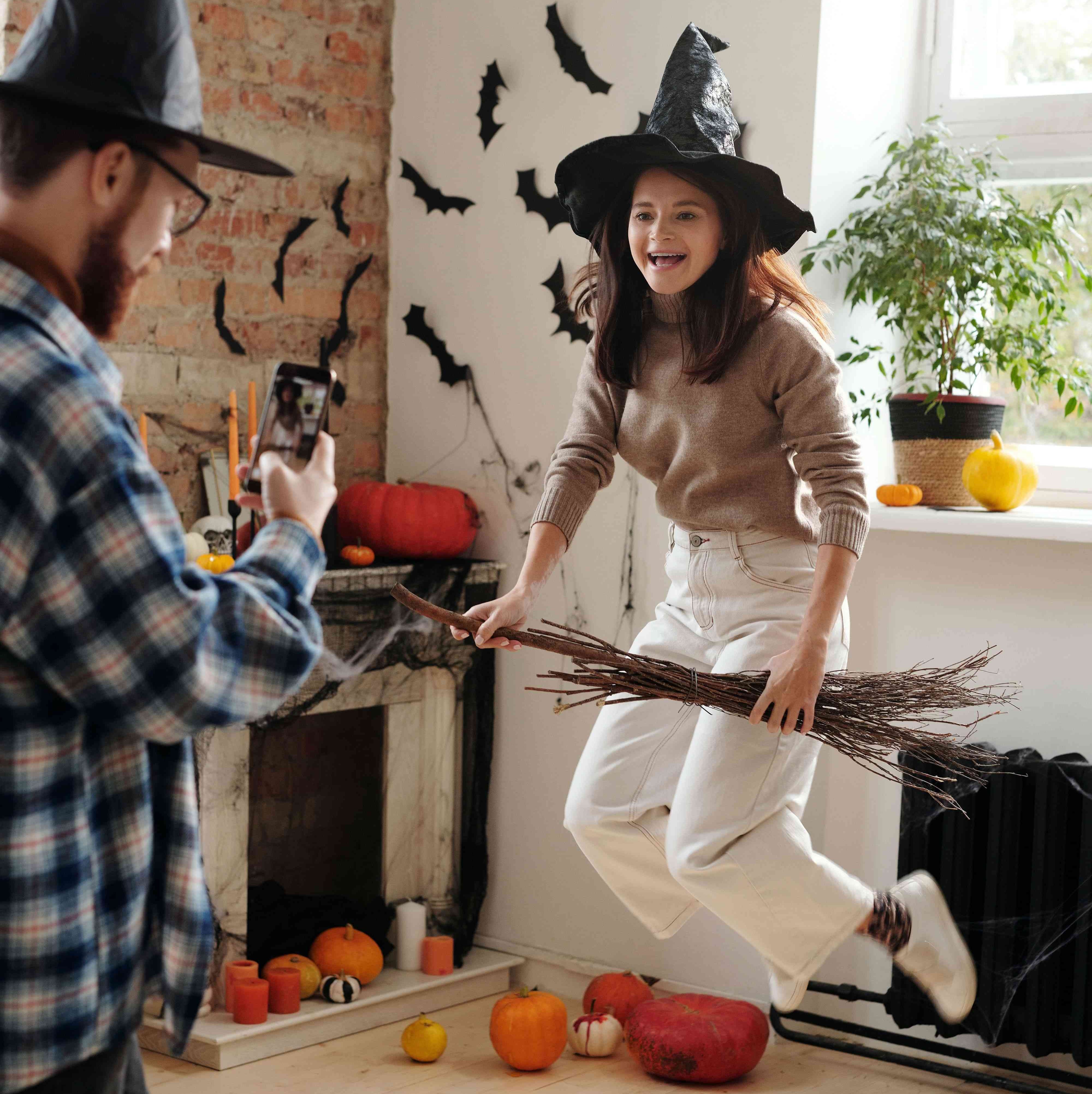 Person taking picture of another person on a broom next to Halloween decorated wall