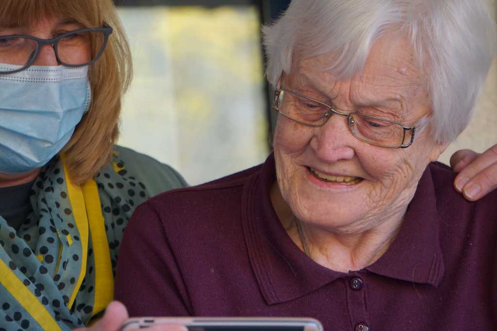 Image shows a person spending time and sharing some content on their mobile phone with an older adult