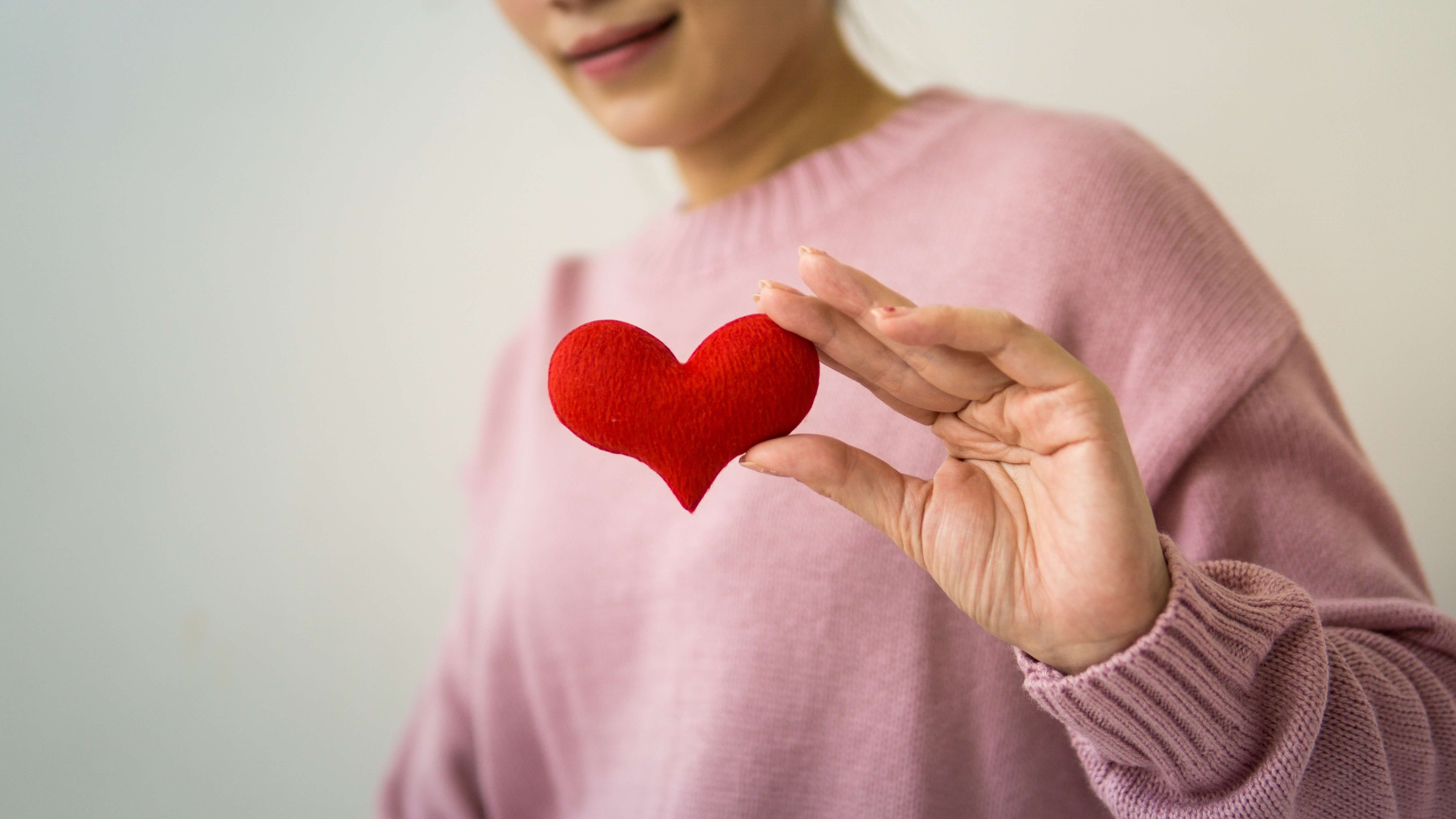 Person in pink sweater holding a picture of heart in their hand