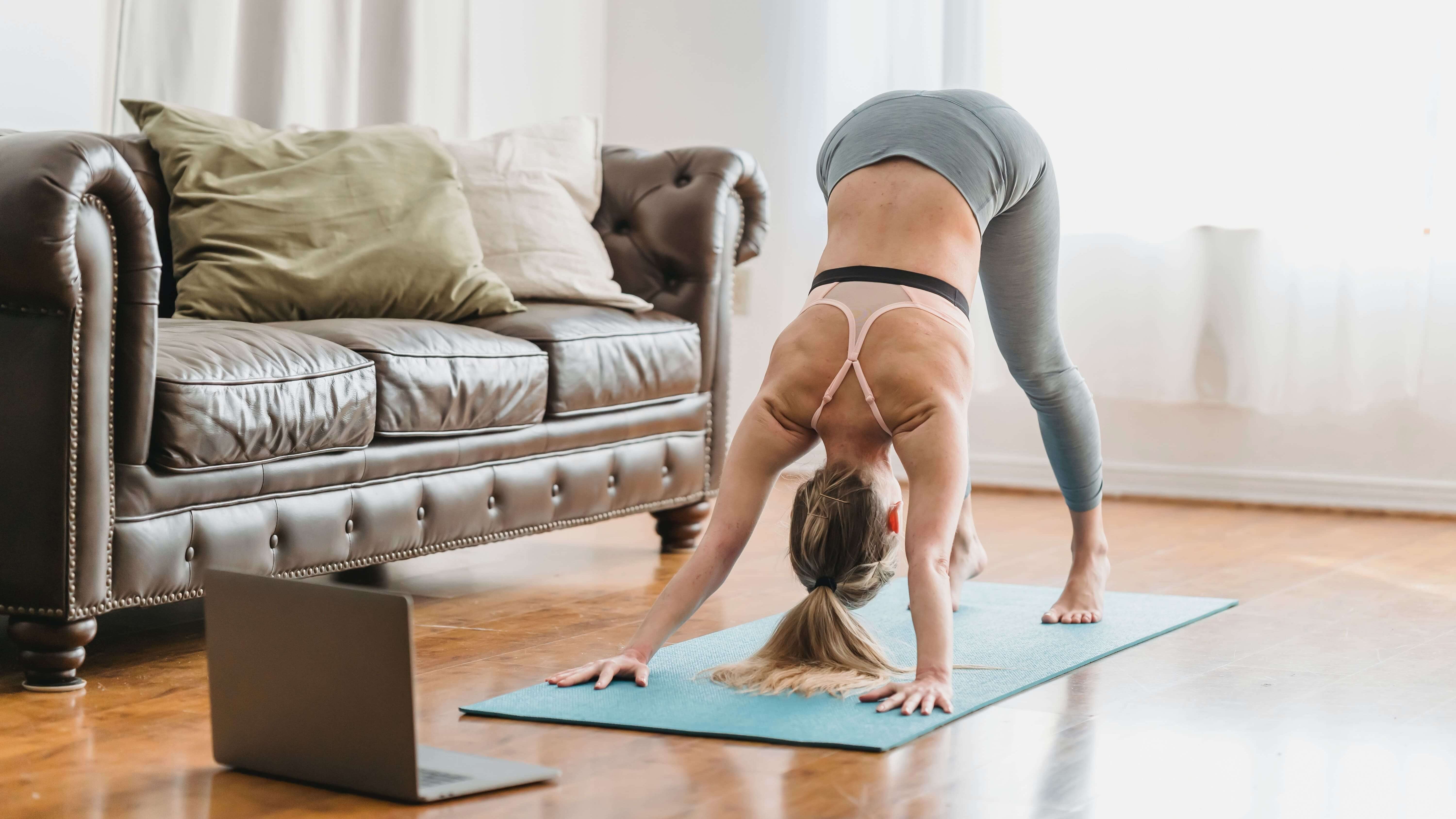 Person on the yoga mat in front of the laptop, participating in online yoga class