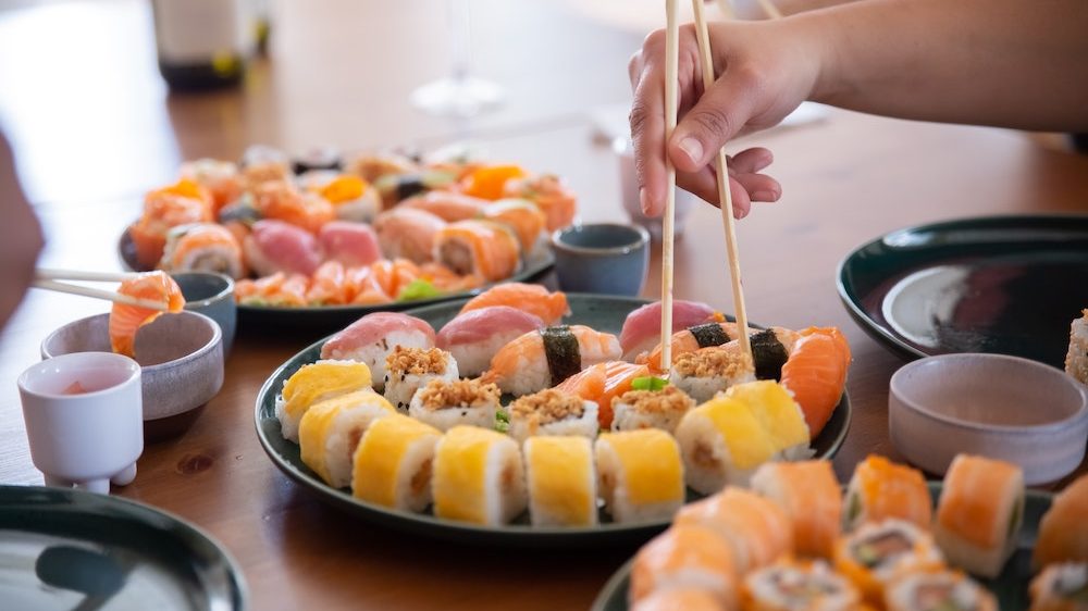 Several sushi sets on the table and a person with chopsticks 