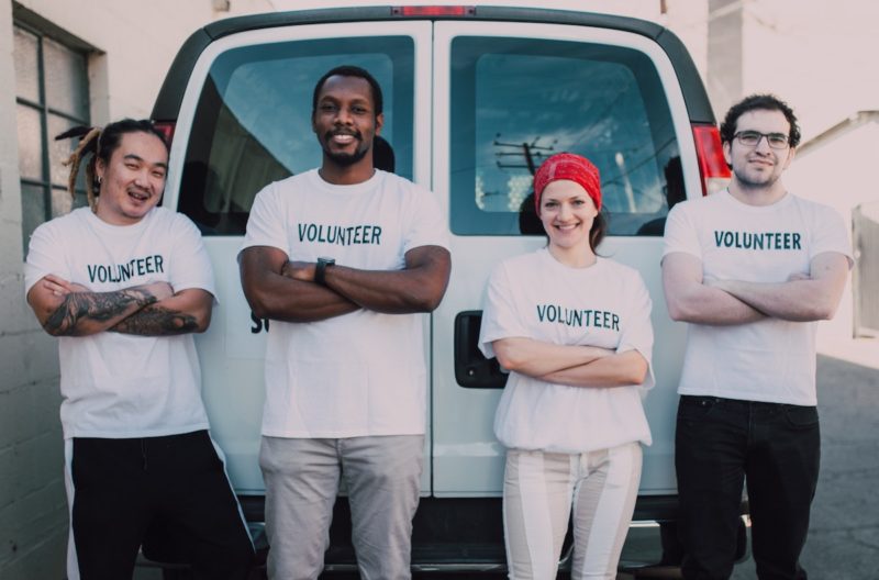 A group of employees in t-shirts that say volunteer, smiling, while taking pictures during a corporate volunteering event
